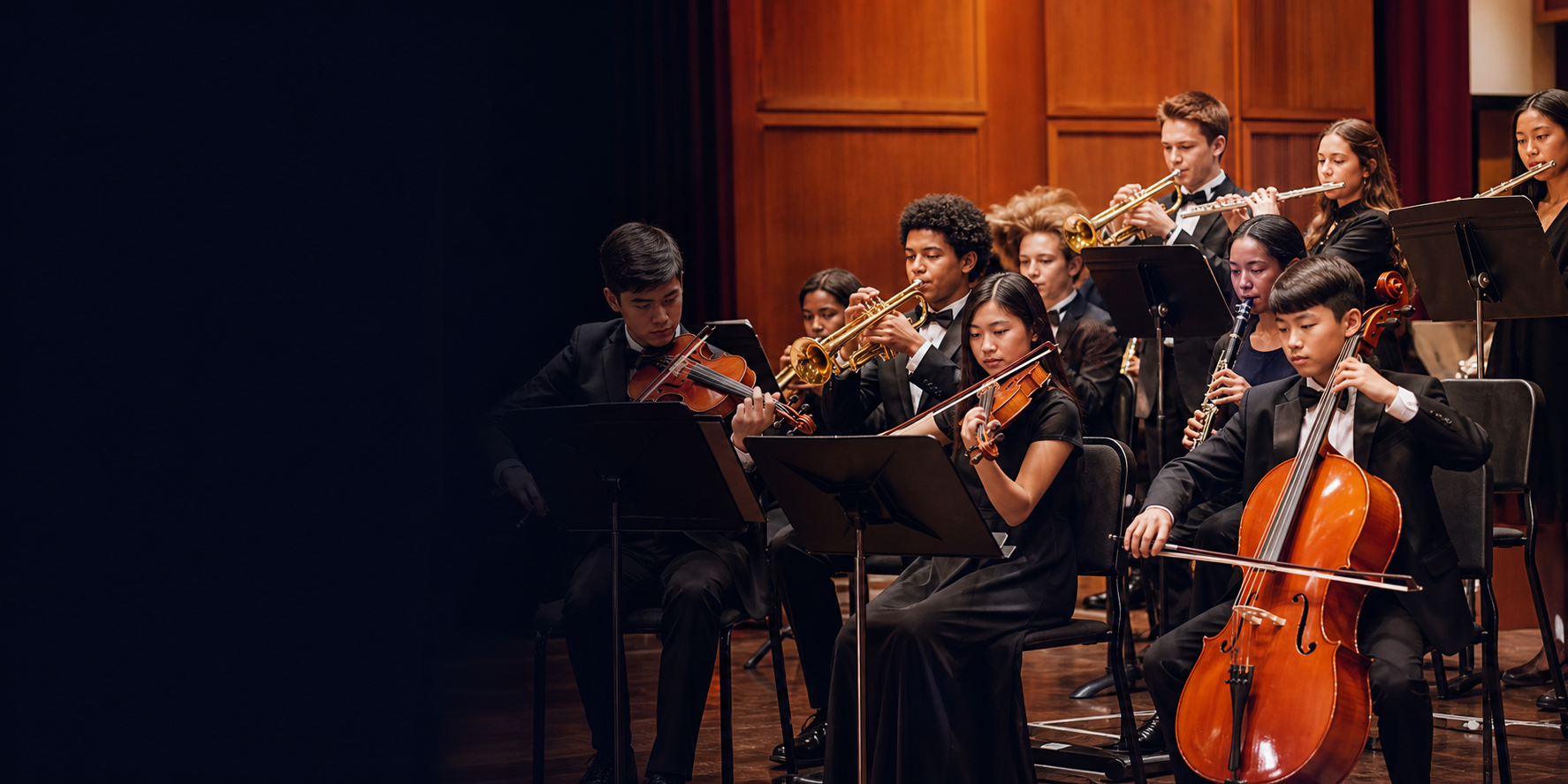Students performing orchestra and band music on a school auditorium stage